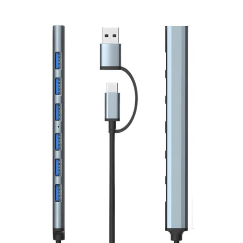 Un hub USB-C gris de aluminio muestra siete puertos USB 3.0 azules y dos conectores laterales con cable negro en fondo blanco.
