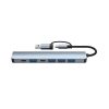 Un hub gris de aluminio con cable USB-C muestra una conexión macho USB y siete puertos, incluidos varios USB y dos USB-C, sobre fondo blanco.