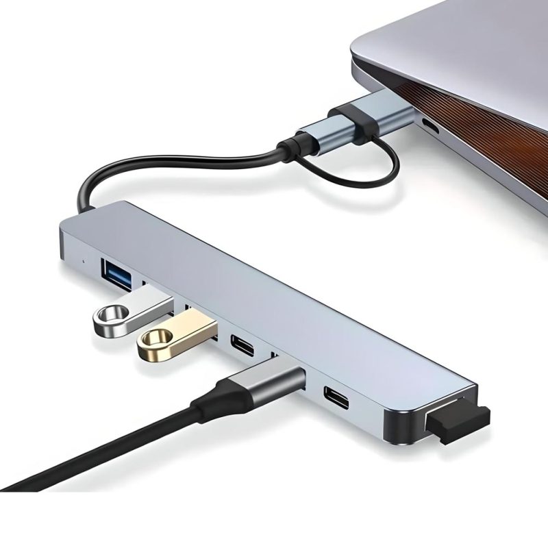 Un hub USB-C gris de aluminio conecta un portátil y muestra puertos USB-A, USB-C y cable corto con diseño compacto para ampliar la conectividad.