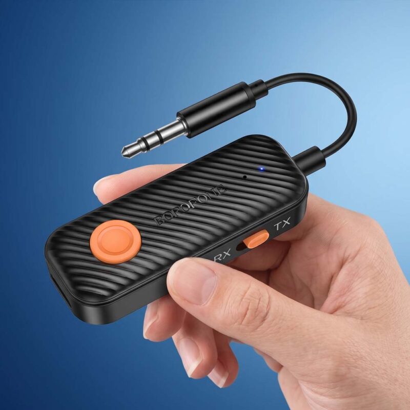 Borofone BC62 negro con conector jack de 3,5 mm, botón naranja y luces LED, sostenido con la mano sobre un fondo azul limpio.
