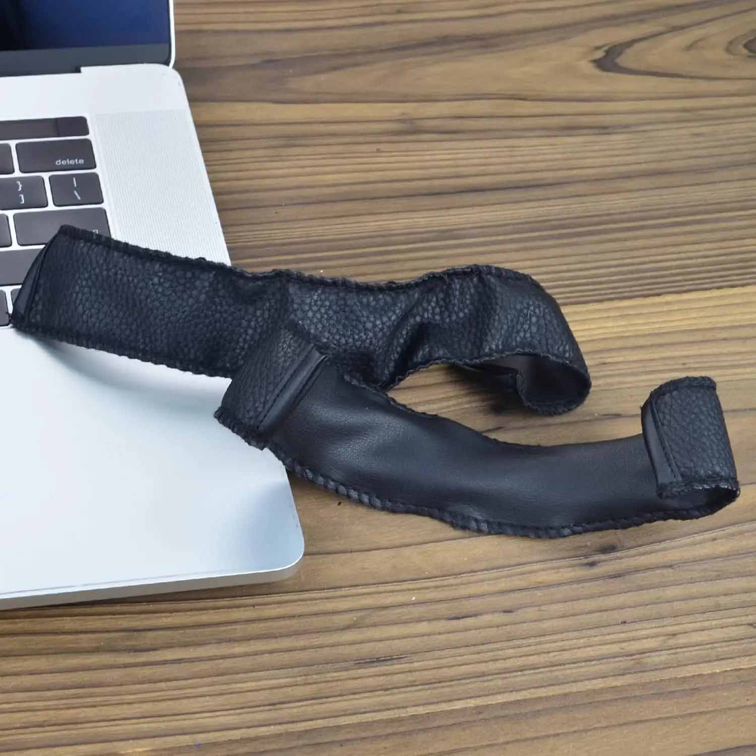 Una diadema negra de repuesto para audífonos Marshall Monitor descansa sobre una mesa de madera junto a un portátil plateado abierto.