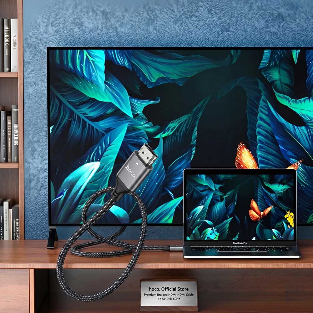 Un cable Hoco USB-C a HDMI de 2 metros conecta una MacBook Pro a una pantalla grande con fondo tropical en alta definición 4K.