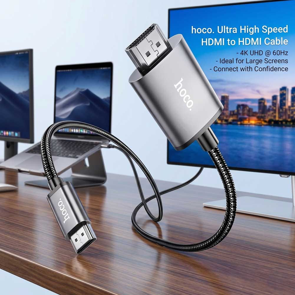 Un cable Hoco USB-C a HDMI de 2 metros con recubrimiento trenzado negro conecta un portátil a una pantalla 4K, con conectores metálicos y cuerpo gris.
