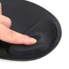 Un mouse pad negro con apoyo de gel para la muñeca muestra una superficie acolchada y base antideslizante mientras un dedo presiona su borde.