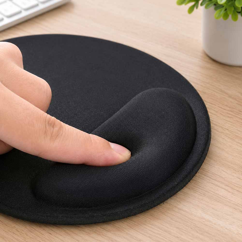 Una mano presiona el apoyo de gel negro de un mouse pad ergonómico sobre una mesa de madera, con base antideslizante y borde reforzado.