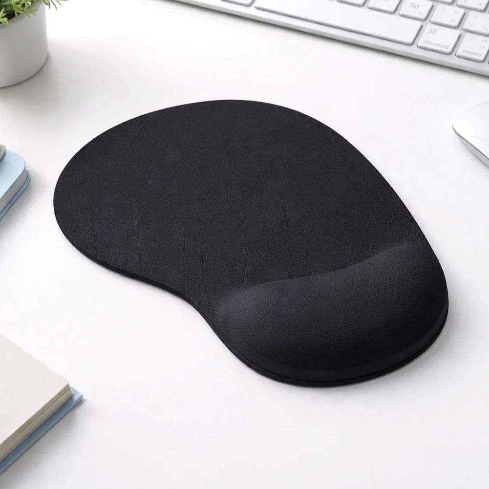 Sobre un escritorio blanco, un mouse pad negro ergonómico con apoyo gel para la muñeca destaca por su base antideslizante y forma compacta y redondeada.