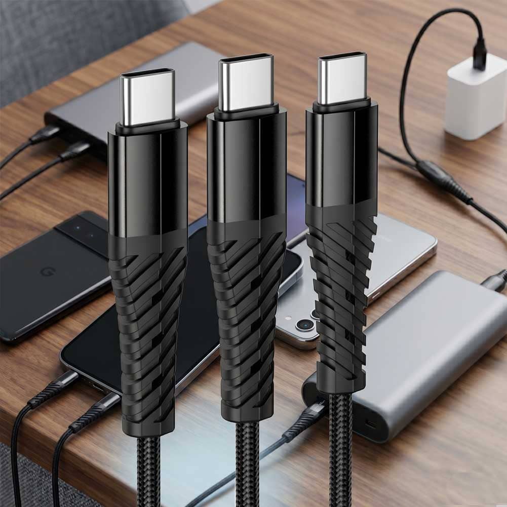 Un cable Hoco X123 negro con conector USB-C doble aparece sobre un escritorio con varios dispositivos cargándose y una batería portátil.
